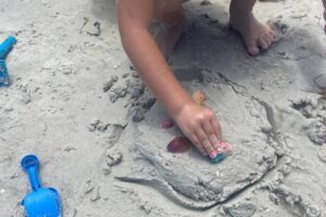 Ella makes a sand "pie" and decorates it with shells