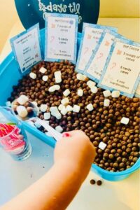 child's hand reaching into hot cocoa sensory bin