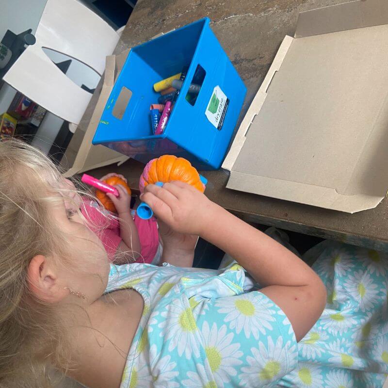 Ella painting a pumpkin with a paint stick.