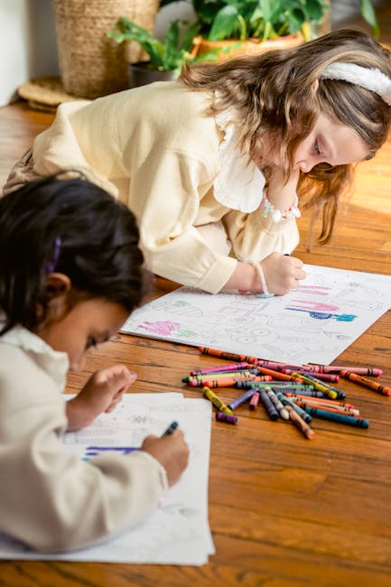 Two girls concentrating on drawing with crayons on the wooden floor.