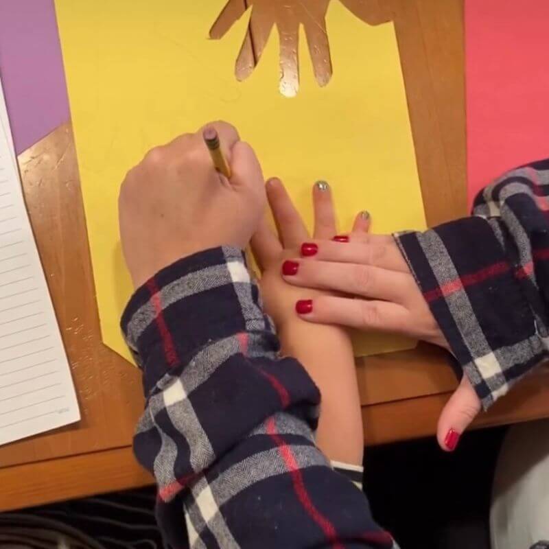 adult tracing child's hand on construction paper