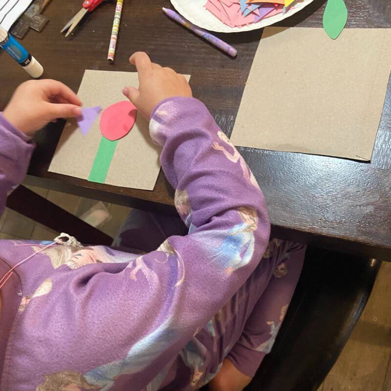 child creating a construction paper flower on cardboard