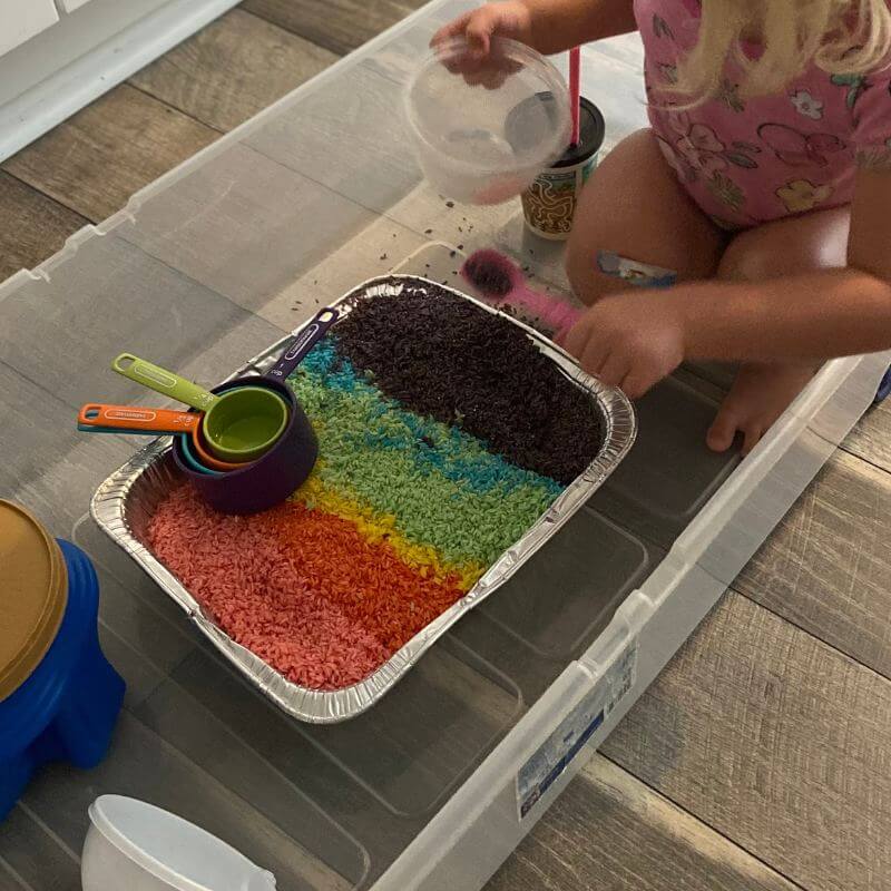 toddler playing with rainbow rice