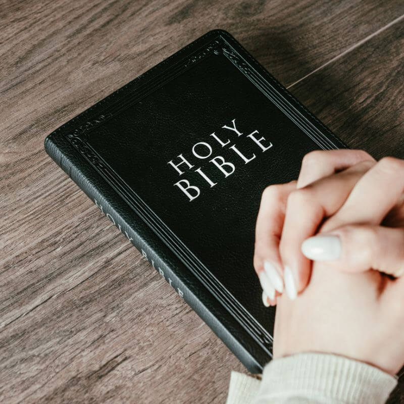 hands folded praying on top of bible